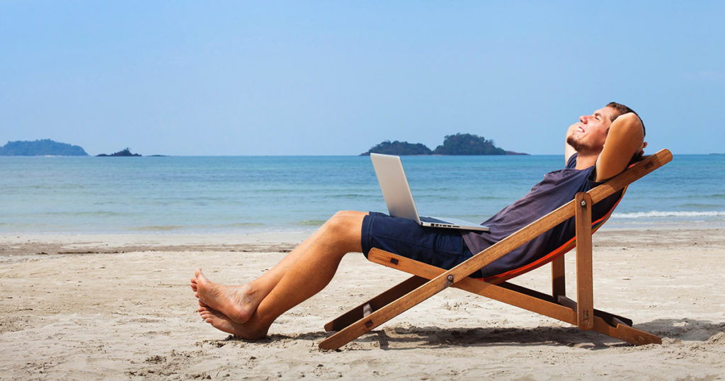 Man sitting on beach reclining with laptop